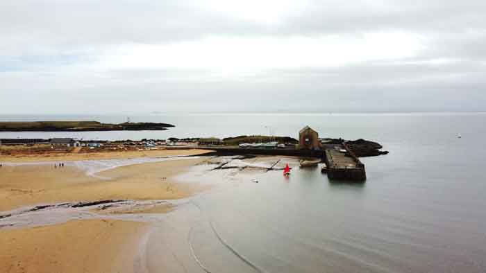 Beautiful view of the pier and a small house in Elie Harbour, Scotland, with a sailing yacht and a motorboat on the water.